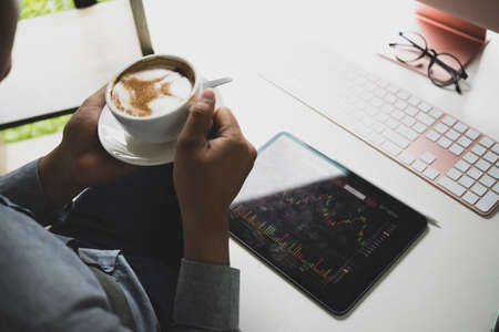 Computer laptop, coffee cup, books and houseplant on wooden desk.