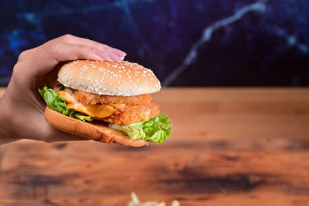 Delicious fish burger with fresh vegetables and cheese on wooden table.の写真素材