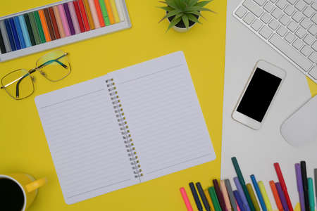 Notepad, smart phone, glasses and smart phone and colored crayons on yellow background.の写真素材