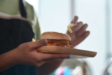 Woman holding crispy fish burger
and eating fried potatoes .の写真素材