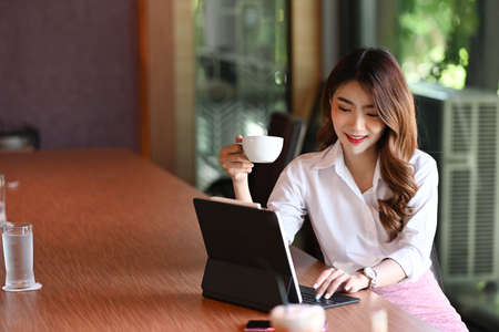 Portrait beautiful businesswoman holding coffee cup and working with computer tablet.の写真素材
