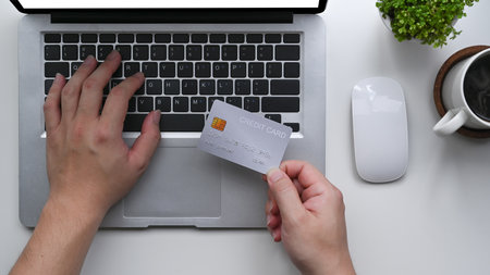 Man holding credit card and using laptop computer for making payment online.