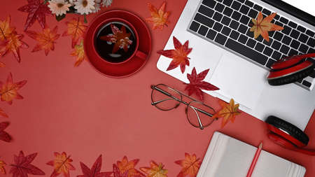 Above view laptop computer, glasses, coffee cup, maple leaves and notebook on red background.の写真素材