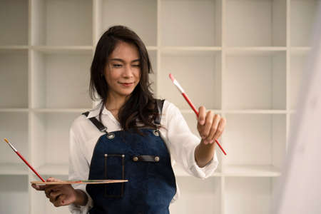 Cheerful female Artist painting picture at the modern art studio.