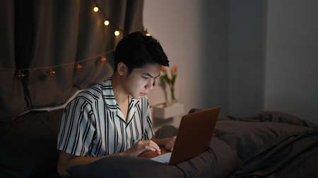 Young Asian man working with computer laptop on his bed at late night.の写真素材