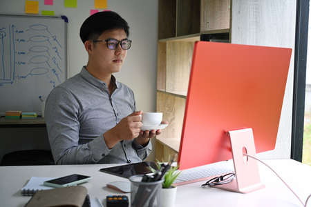 Thoughtful businessman drinking coffee and analyzing financial data on computer.の写真素材
