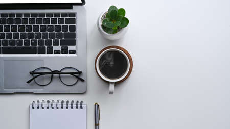 Simple workplace with computer laptop, coffee cup, glasses, notebook and plant on white desk.の写真素材