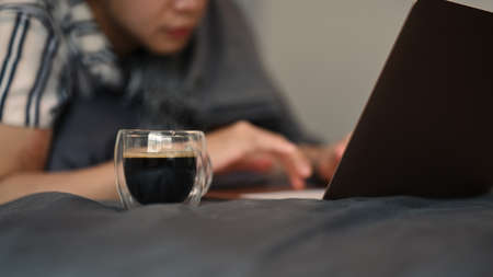 Casual man drinking hot coffee and using laptop computer on his bed in the morning.の写真素材