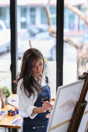 Young female artist painting picture on canvas in a creative art studio.