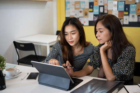 Two Asian women colleagues working together on project with computer tablet at office.の写真素材
