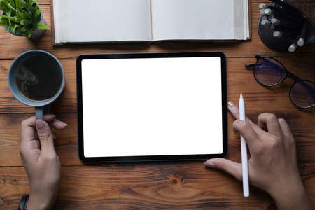Overhead view woman holding coffee cup and working with digital tablet on wooden table.の写真素材