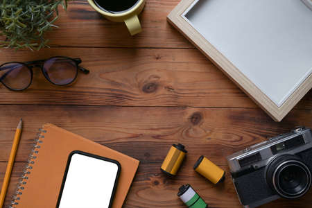 Above view photographer workplace with smart phone, retro camera and glasses on wooden desk.の写真素材