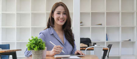 Beautiful female accountant sitting at her workplace and smiling to camera.の写真素材