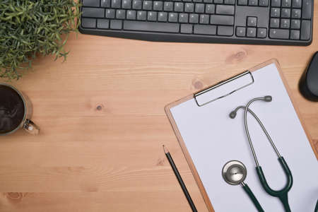 Above view doctor workspace with coffee cup, clipboard and stethoscope on wooden table.の写真素材
