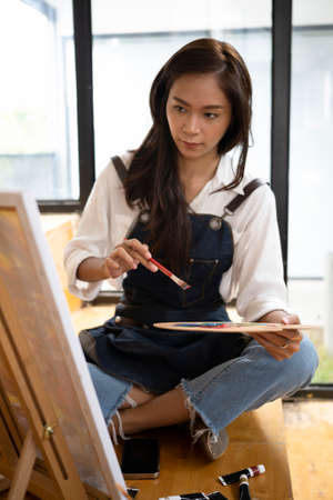 Female artist sitting in her art studio and painting a picture on canvas.の写真素材