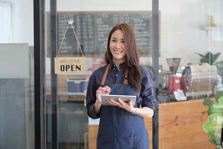 Portrait of friendly female entrepreneur holding digital tablet while standing in her coffee shop.の写真素材