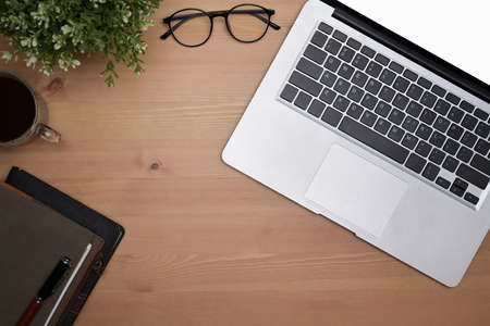 Laptop computer, glasses, coffee cup and notebook on wooden background.