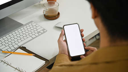 Back view of young man sitting at his workplace and using smart phone.
