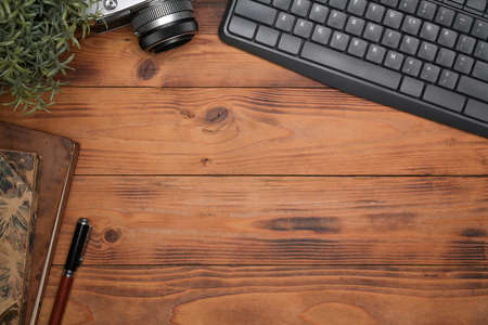 Above view camera, notebook, houseplant and keyboard on wooden background.