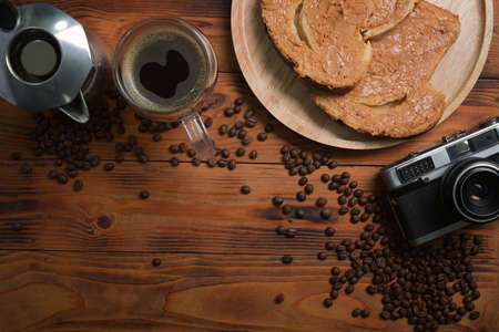 Top view retro camera, coffee cup and toast bread with peanut butter on wooden table.
