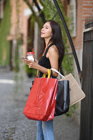 Portrait of female traveler holding her digital camera and shopping bags standing at outdoor.