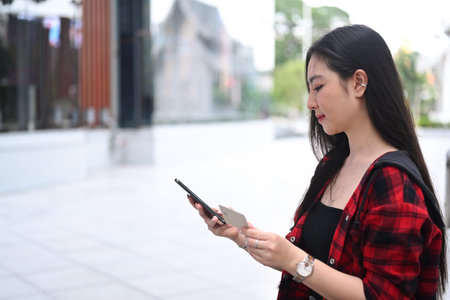 Young Asian woman using smart phone while standing on a city street.の写真素材