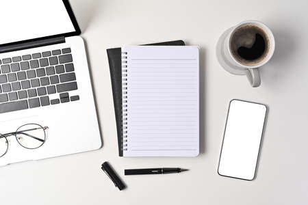 Top view smart phone, laptop computer, notebook and coffee cup on white table.