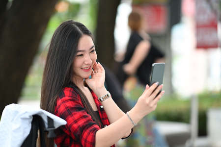 Young Asian woman having video call with her friends on smart while sitting outdoor in the city.の写真素材