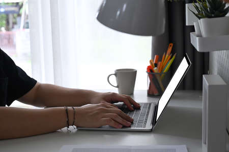 Cropped shot young man making note on notebook and using laptop computer.