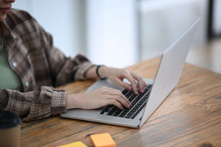 Cropped shot female designer using laptop computer on wooden table.