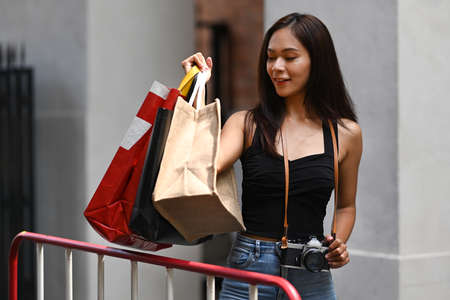 Young woman traveler taking picture with her camera while sitting outdoors with shopping bags.