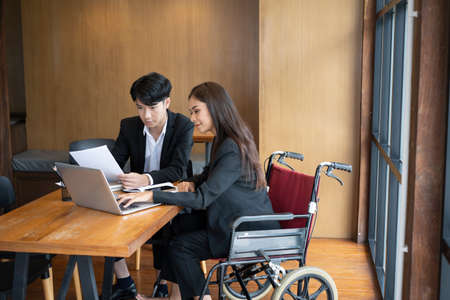 Smiling handicapped young woman working with her colleague in office.の写真素材