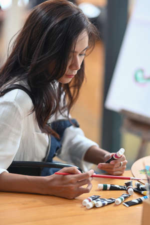 Pretty female artist painting on canvas in bright daylight studio.