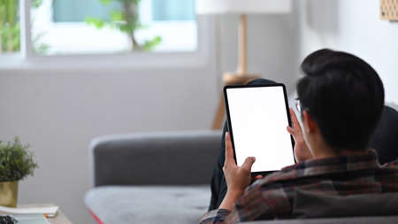 Back view casual man sitting on comfortable sofa and using digital tablet.