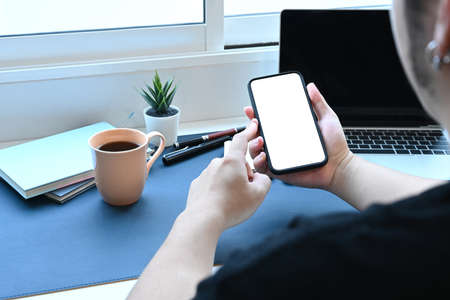 Over the shoulder view of young man sitting at workplace and using smart phone.の写真素材