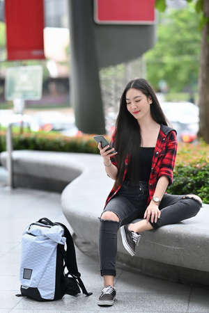 Young Asian woman sitting in city park and using smart phone.の写真素材
