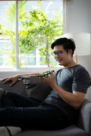 Young man recording audio message or calling on smartphone while sitting in living room.
