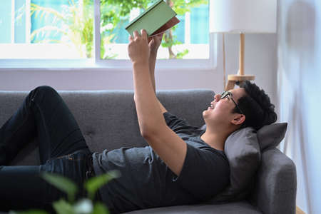 Man lying on comfortable sofa in living room and reading a book.の写真素材