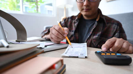 Cropped shot man using calculator and managing household finances in living room.の写真素材