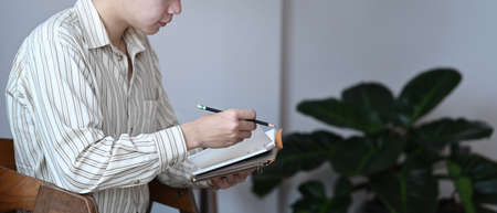 Portrait of handsome businessman holding pen and writing information on notebook.の写真素材