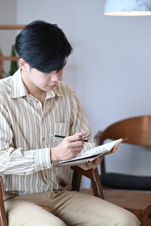 Portrait of handsome businessman holding pen and writing information on notebook.の写真素材