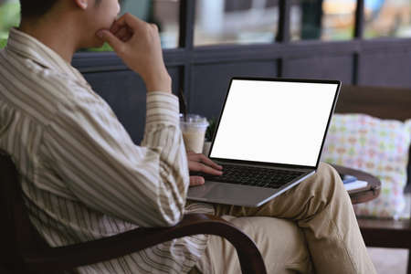 Side view young man holding coffee cup and working with laptop computer in cafe.の写真素材