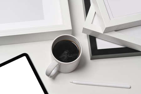 A cup of coffee, digital tablet and empty picture frames on white background.