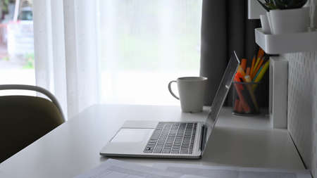 Side view computer laptop, coffee cup and pencil holder on white table.