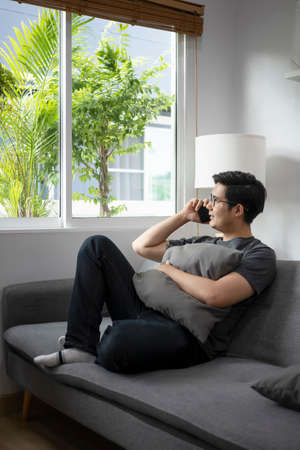 Happy casual man sitting on sofa and talking on mobile phone.の写真素材