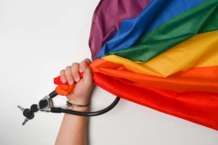 Man hand holding LGBT pride flag with Metal chain and padlock. Love and freedom concept.の写真素材