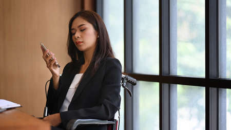 Disabled businesswoman in wheelchair working in office.の写真素材