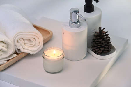 Burning wax candle, towels and shampoo bottles on white table.の写真素材