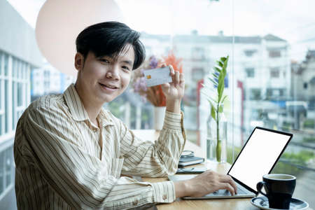 Cheerful young Asian man holding credit card and smiling to camera.の写真素材