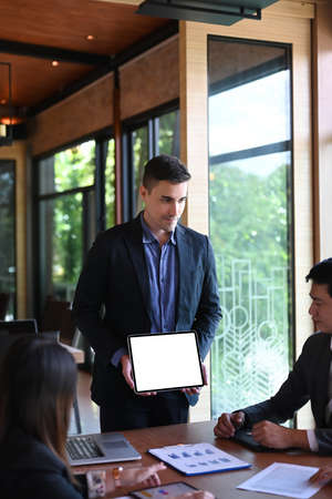 Handsome businessman holding digital tablet and presenting new project to business partners in modern office.の写真素材